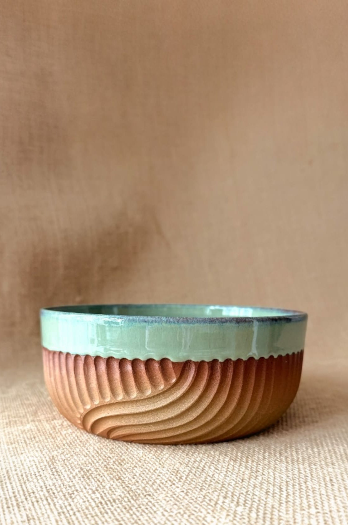 Ceramic bowl with wavy design and green rim on a beige background